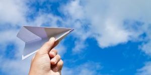 hand with paper plane against blue sky